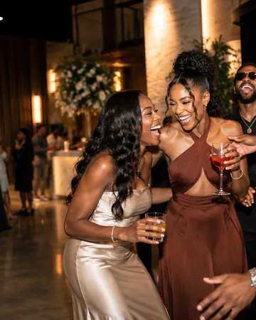 Four guests laughing together at an evening reception, warm light behind them.