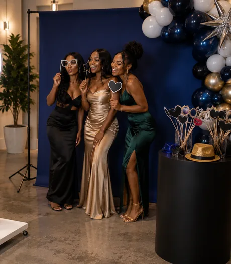 Three guests in evening gowns laughing together against a navy backdrop at a formal event.