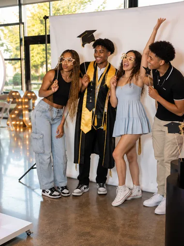Graduates in caps and gowns cheering in front of a bright backdrop.