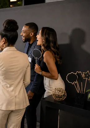 Three colleagues talking and laughing at a rooftop company event.